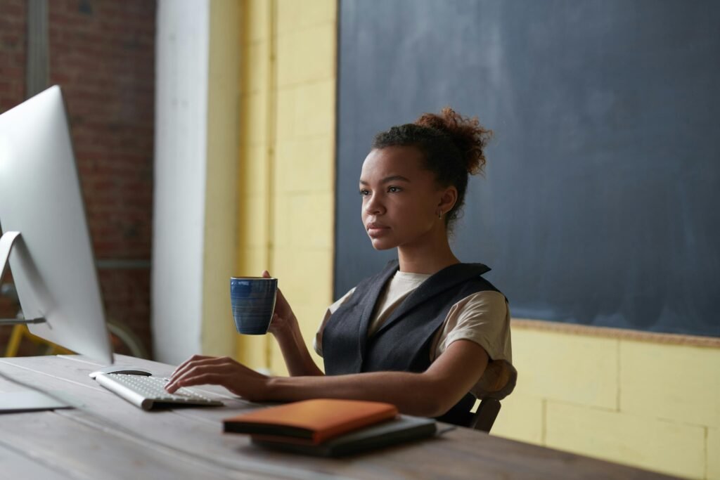 A professional young woman concentrating on work at a desk with a computer and coffee cup in hand.