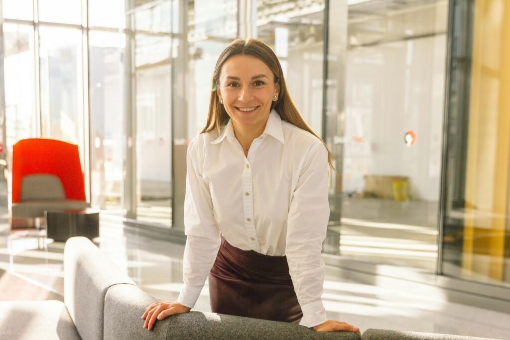 Smiling woman in white blouse posing confidently in a modern office space.